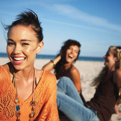 Young women smiling on beach, portrait, close-up (focus on foreground)