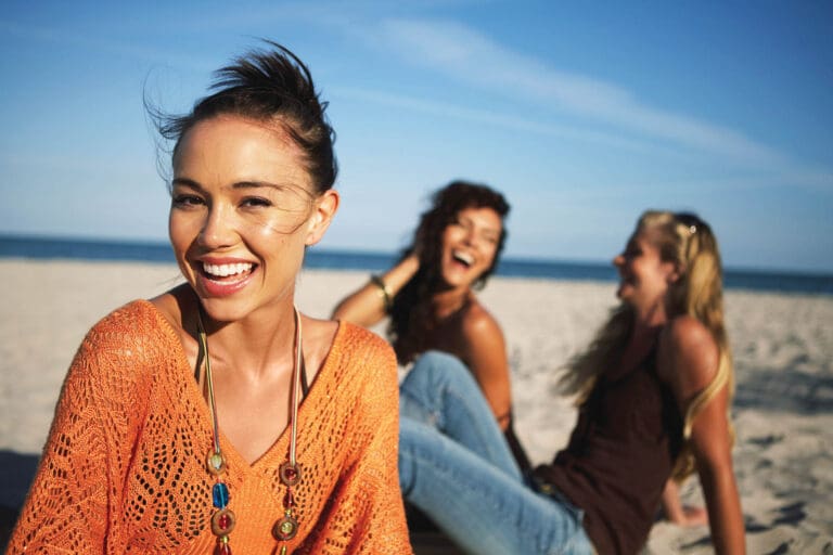 Young women smiling on beach, portrait, close-up (focus on foreground)