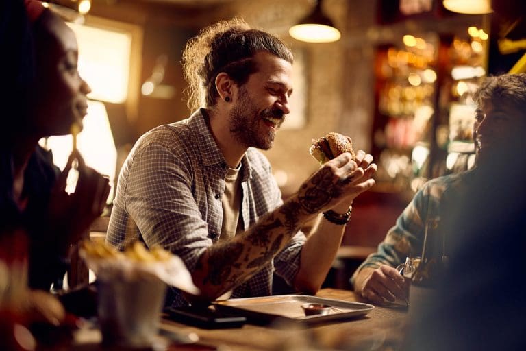 Cheerful man eating burger while gathering with friends in a bar.