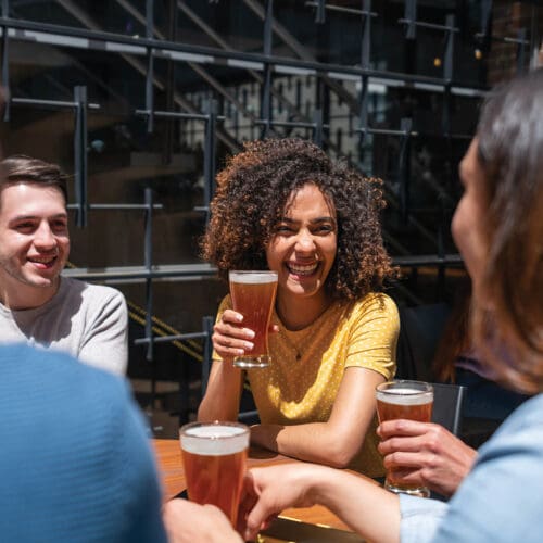 Happy Latin American woman having fun at a bar drinking beers with a group of friends - lifestyle concepts