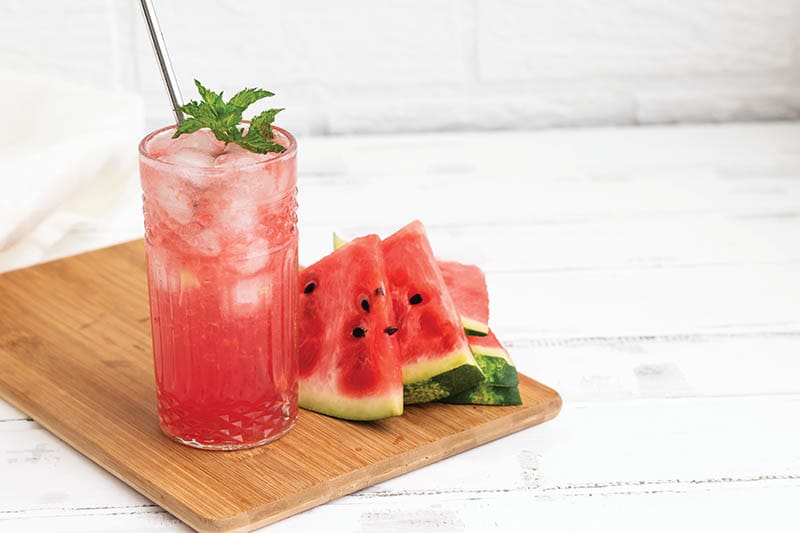 Watermelon smoothie or iced juice with watermelon slices and mint leaf on a white wooden background.